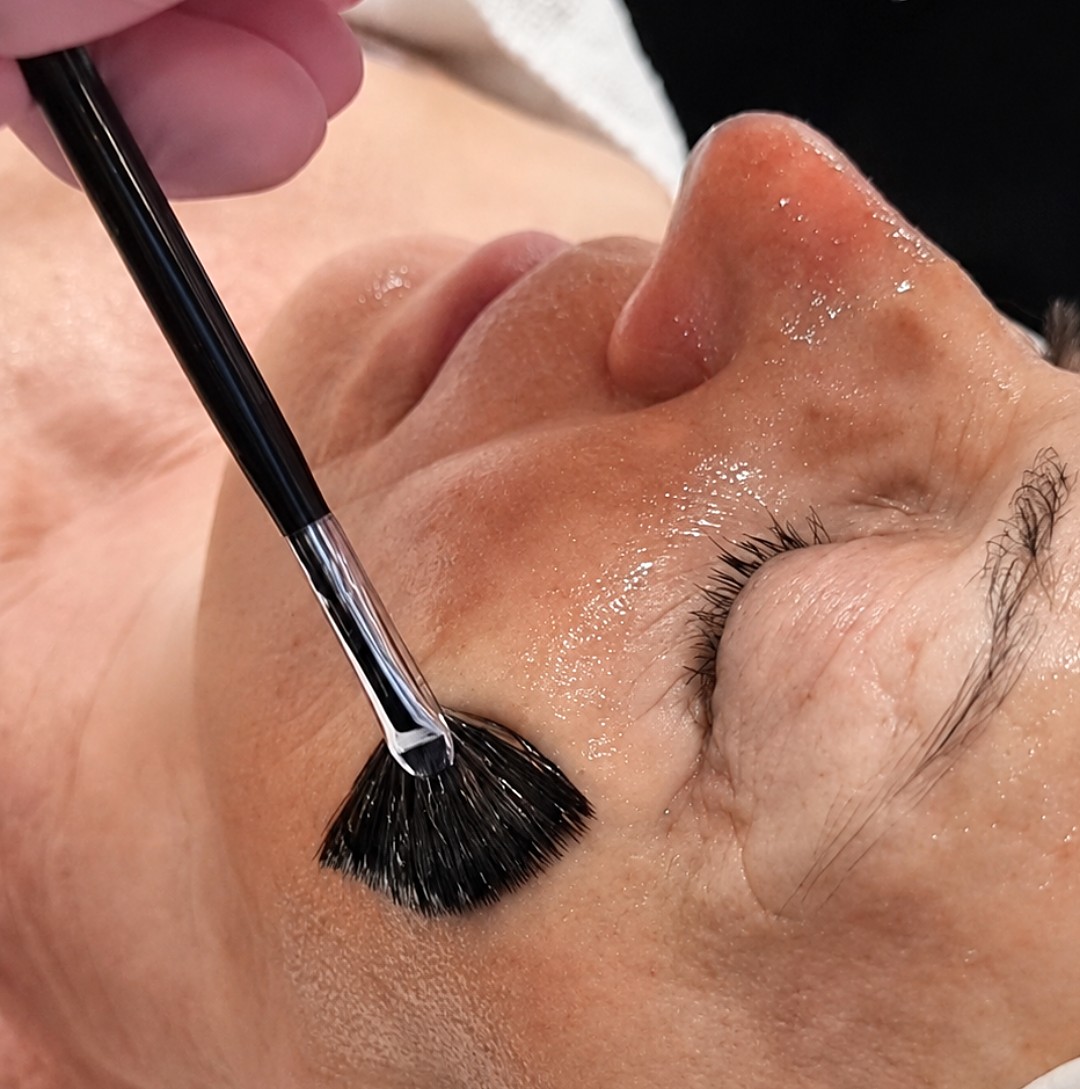 Ein Fächerpinsel trägt ein Peeling auf Nase und Wange auf